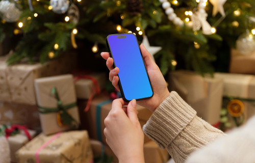 Hand holding a phone mockup next to the Christmas tree with gifts
