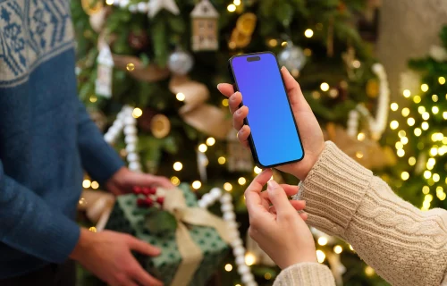 Woman holding an iPhone mockup next to the Christmas tree
