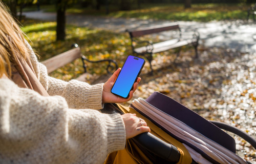 Woman holding an iPhone while walking in a park mockup