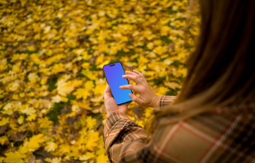 Woman typing on an iPhone 14 Pro in autumn theme mockup