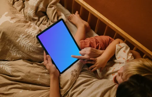 Woman with a child typing on an iPad mockup in bed
