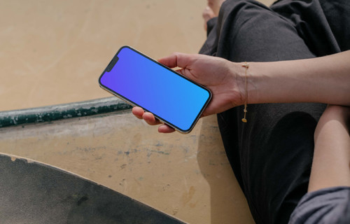 iPhone 13 Pro mockup held by a user seated next to a skateboard