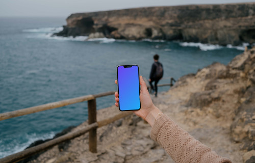 iPhone 13 Pro mockup held by a user at a coastline