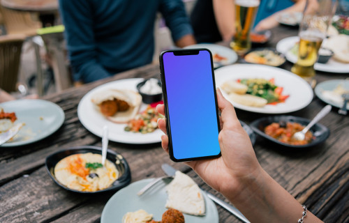 iPhone mockup in a user’s hand at dinner table
