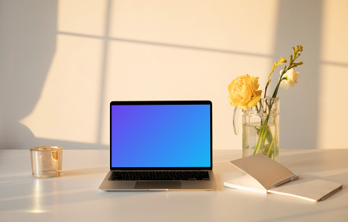 MacBook mockup sobre una mesa con un jarrón de flores y un libro de ejercicios al lado.
