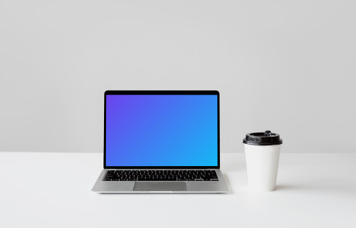 MacBook mockup sobre una mesa blanca con un vaso de café desechable al lado