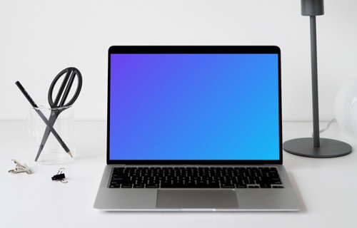 MacBook mockup sobre una mesa blanca con una lámpara de mesa negra al lado