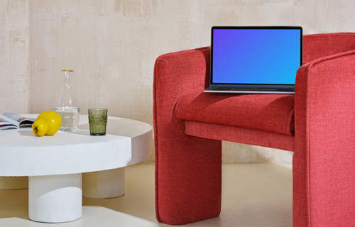 MacBook mockup al borde de una silla roja con una mesa central al lado