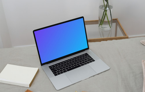 MacBook mockup en una cama con una jarra y cerámica en una bandeja de madera y un cuaderno al lado