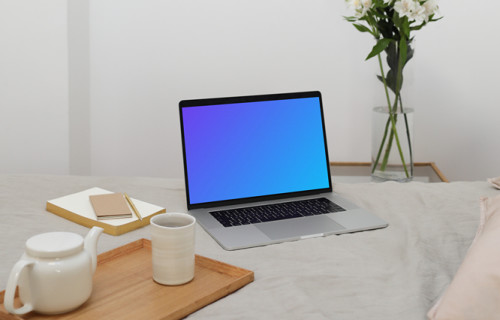 MacBook mockup en una cama con un jarrón de flores en el fondo