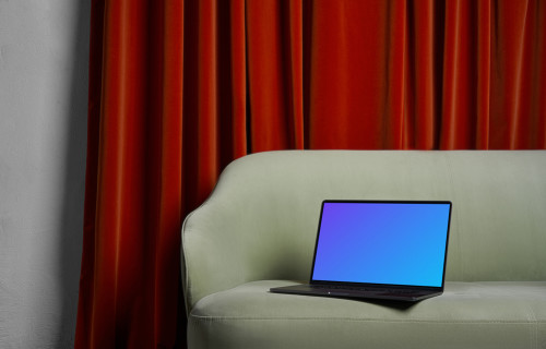 MacBook mockup en un sofá con una cortina marrón de fondo