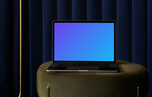 MacBook mockup en un taburete del sofá con una cortina azul de fondo