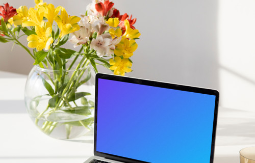 MacBook mockup en una mesa blanca junto a un jarrón de flores en forma de cuenco cerca