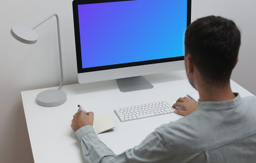 Mockup de un hombre usando un iMac en una mesa blanca en un entorno de oficina en casa