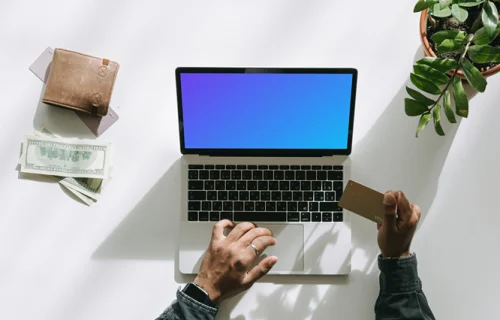 Mockup de Usuario comprando en un MacBook gris junto a algo de dinero y una cartera