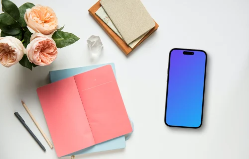 Smartphone mockup next to a pink notepad and flowers