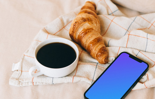 iPhone 12 Pro mockup beside a croissant and a cup of coffee