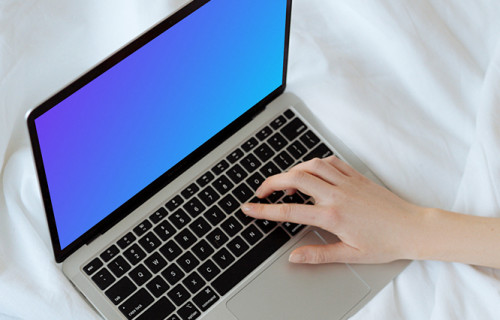 MacBook mockup sobre una cama blanca con un usuario escribiendo en el portátil