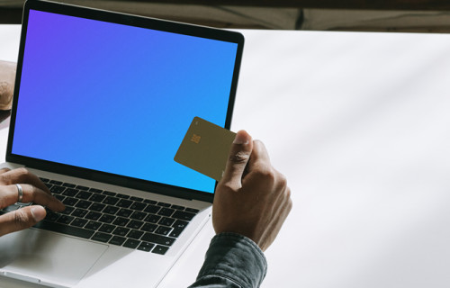 Usuario de MacBook con una tarjeta de débito en la mano mockup.